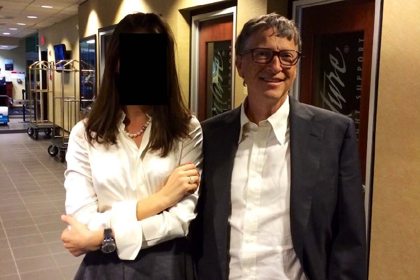 A woman wearing a white shirt has her face blacked out and is standing next to a man smiling