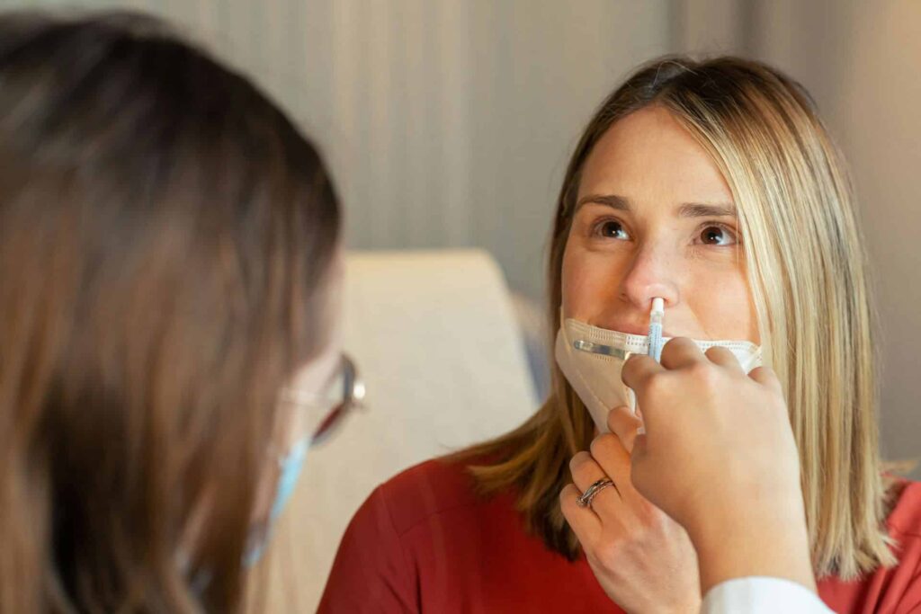 Nasal spray being administered to a woman in a clinical setting.