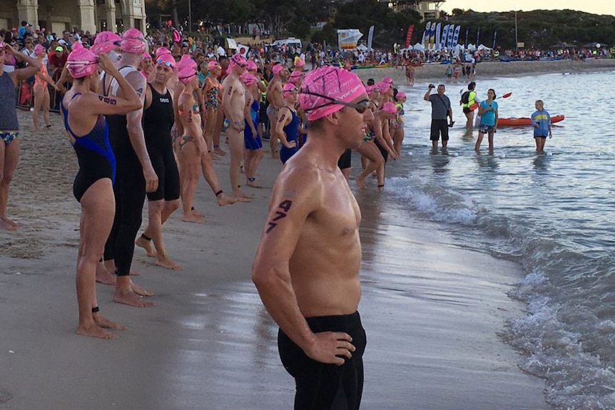 Swimmers in pink bathing caps along the shore at Cottesloe Beach.