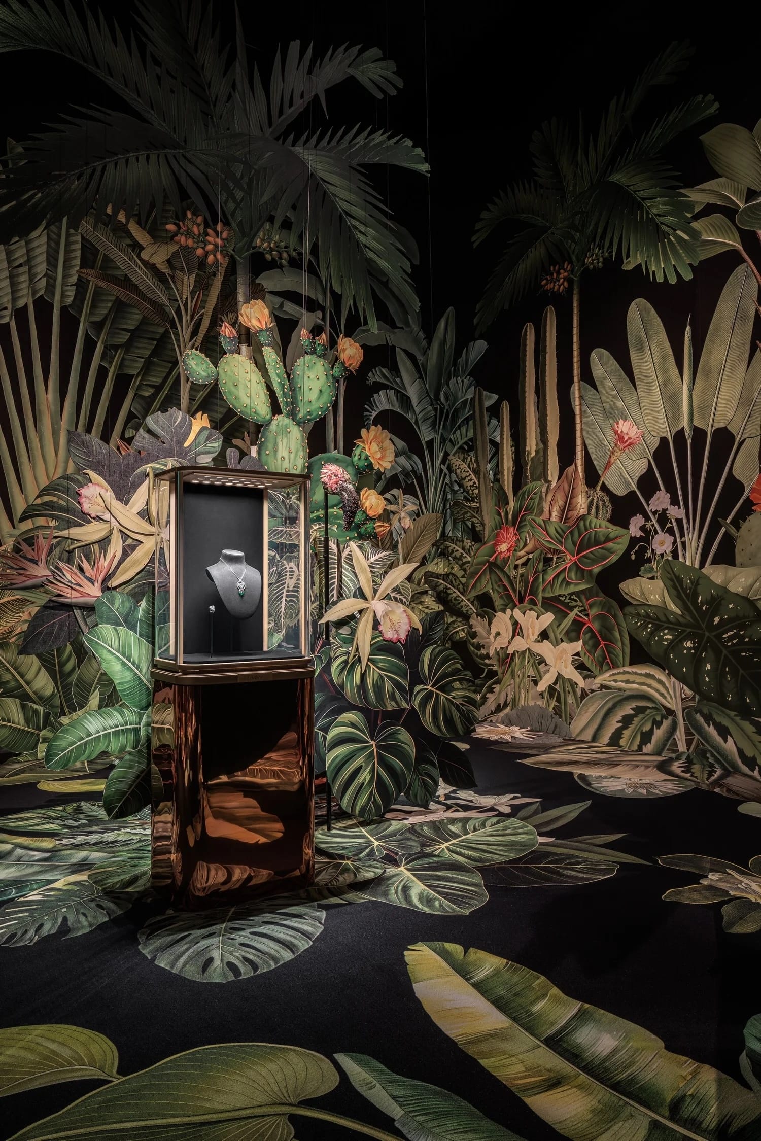 A colorful retail installation for Cartier by Clare Celeste of foliage against a black background, interspersed with cases of jewelry