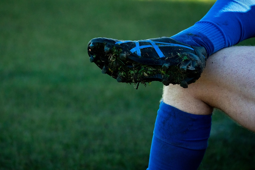 A footballer's leg and boot crossed over his other leg.