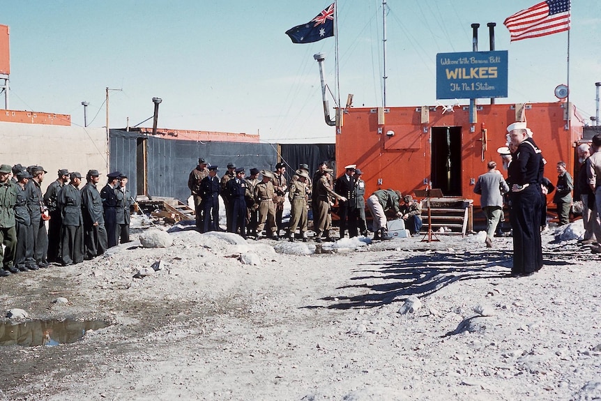 Two groups of men start in uniform outside a research station in Antarctica