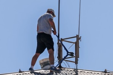 a man on a roof uses bolt cutters on a chain attached to his leg