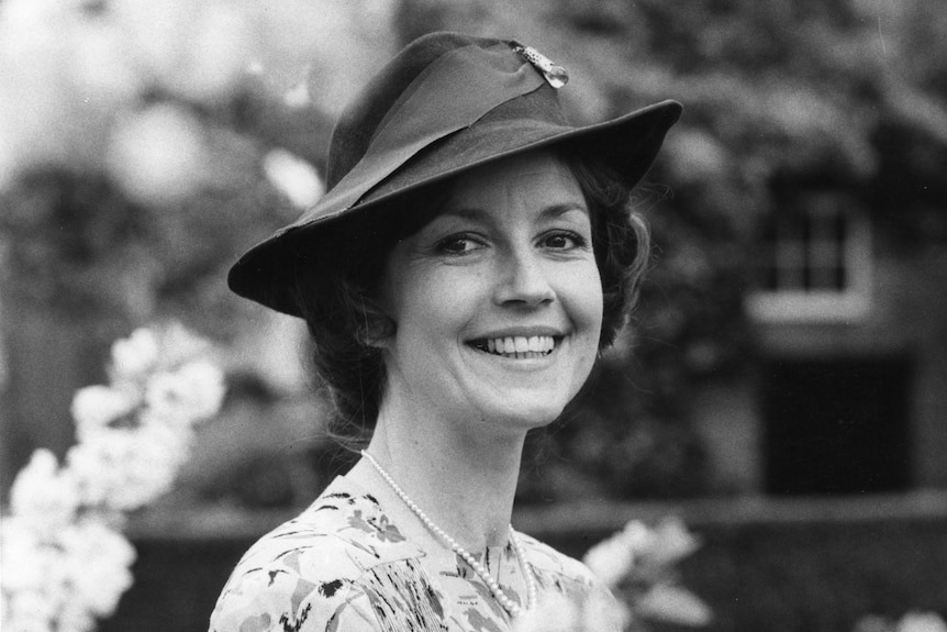 a lady in a dress and hat smiles at the camera