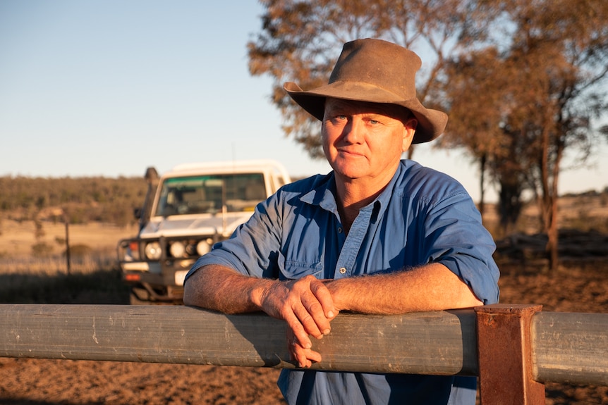 a man with a hat leans on a metal fence