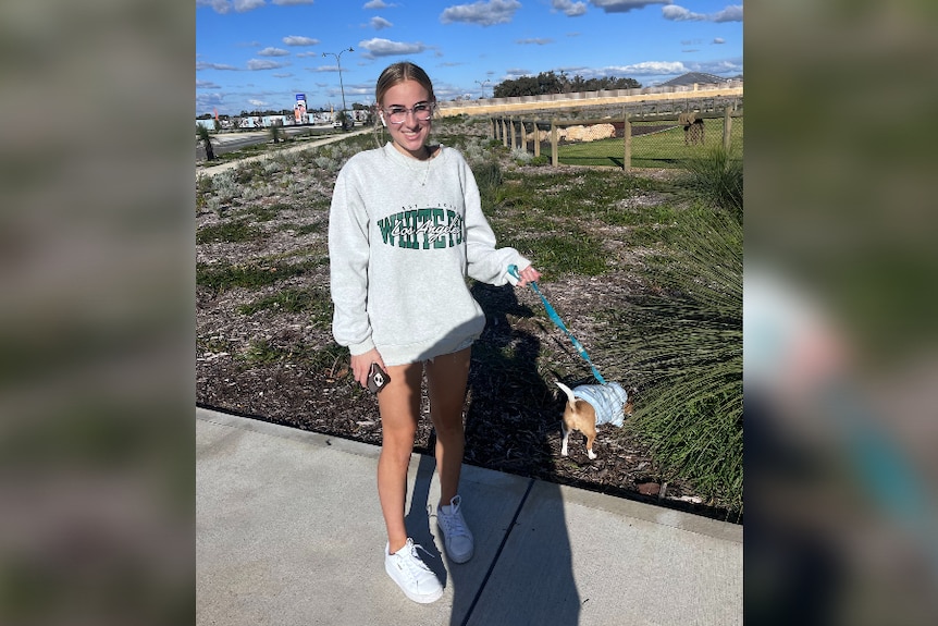 A teenage girl smiles while walking a dog on a lead outdoors.
