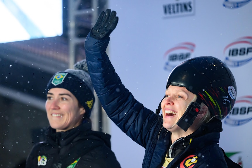 Two women in helmets smile and wave