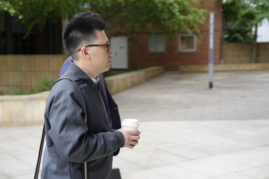 Male Arrives at court with Lawyer dressed in black pants and great jacket holding coffee cup with a brown satchel bag