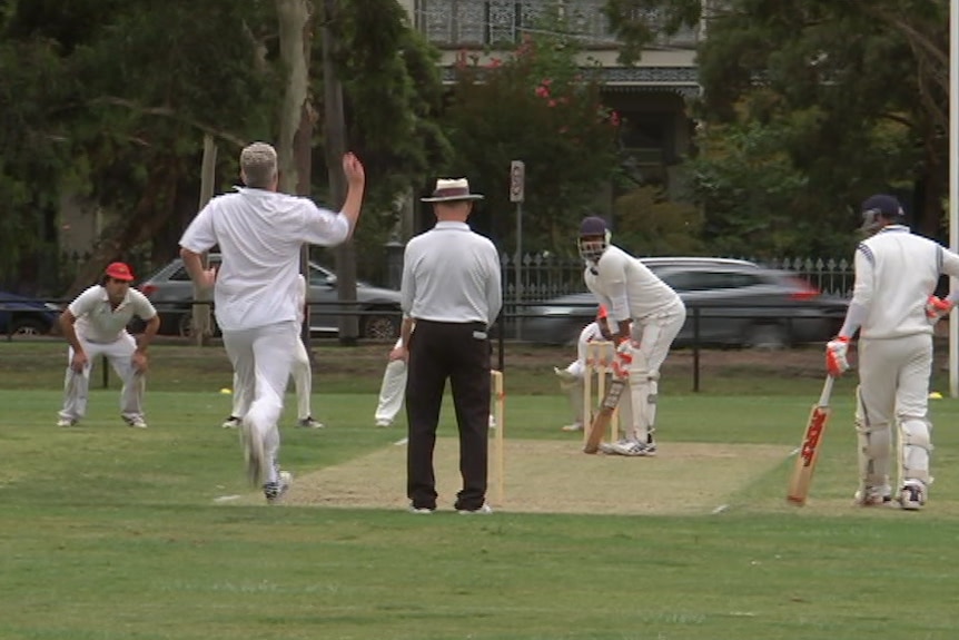 Men dressed in white play cricket.