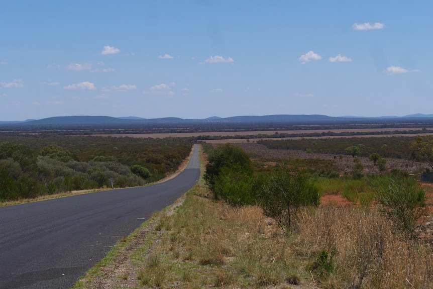 An isolated stretches out into the distance, it is surrounded by low scrub and there are large hills in the background.