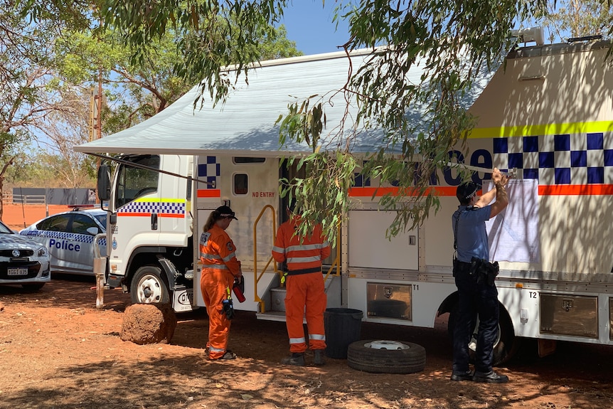 People in uniforms stand around a police van parked in a bush area.