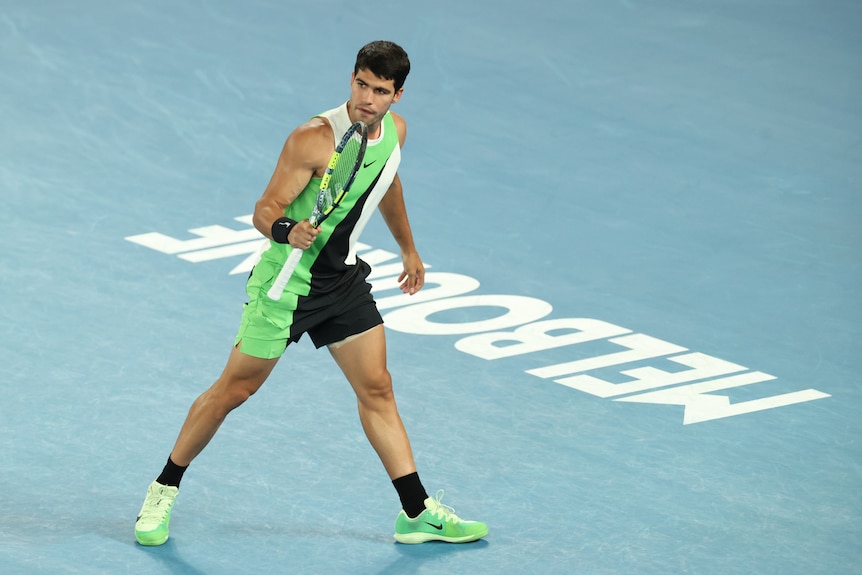 Carlos Alcaraz holds his racquet as he walks past the Melbourne sign in the Australian Open final.