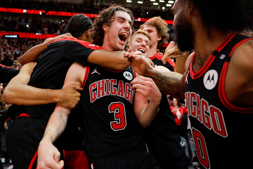 Josh Giddey shouts in joy as Chicago Bulls teammates embrace him after a game-winning NBA shot.
