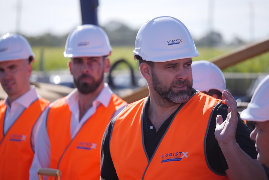 A man in high-vis vest looking backwards in a crowd of people in similar dress.