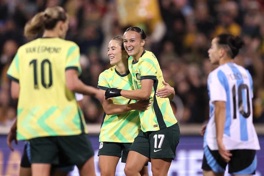 Two players in green and gold celebrate a goal.