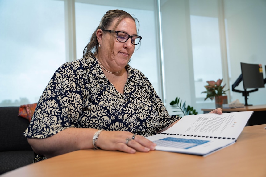 A woman with a serious expression reads an open document. 