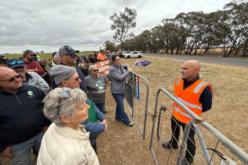 Man talking to a group of people on the other side of a fence