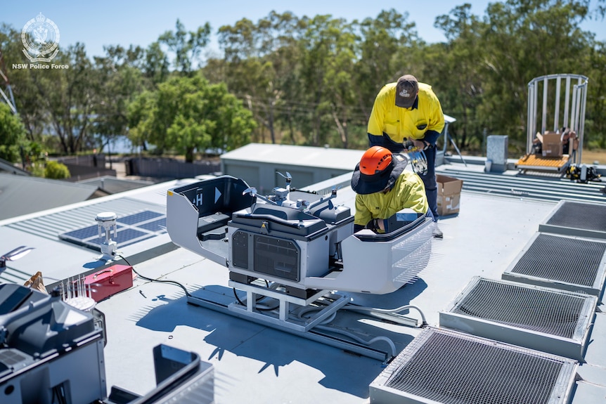 Two workers in hi-vis colothing work on a rooftop drone launch pad.