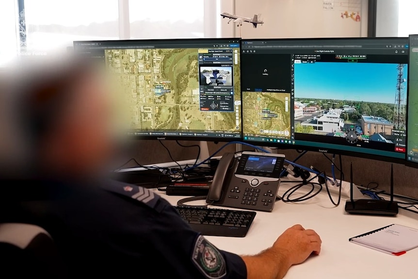 Police officer with features blurred monitors two screens as he operates a drone.