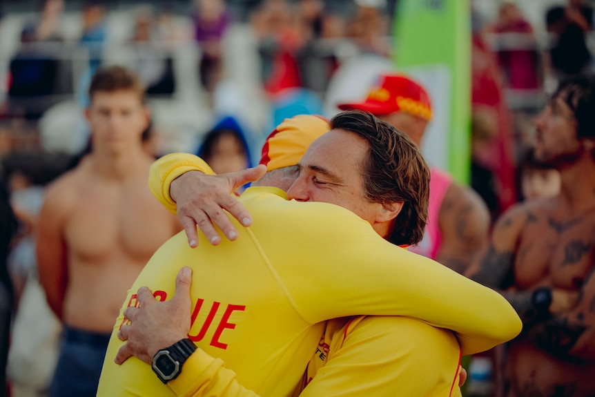 Two lifeguards or life savers in yellow hugging each other in a crowd.
