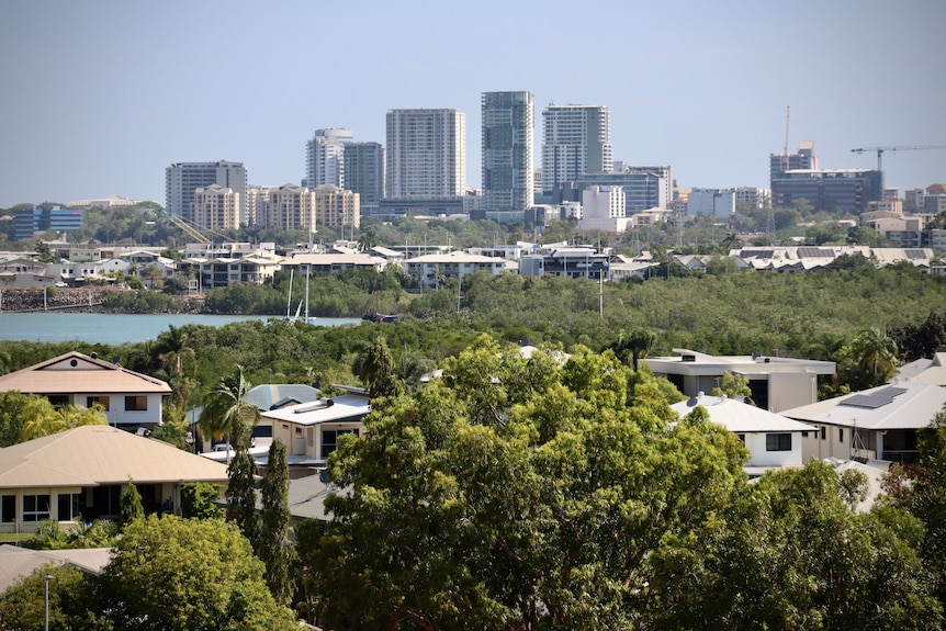 Tall buildings seen from a few kilometres away over leafy suburbs and water.