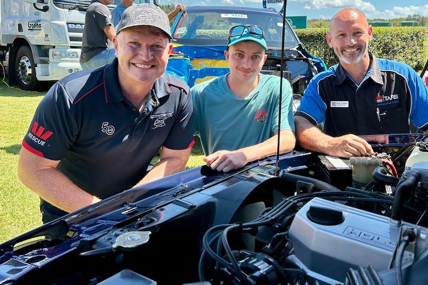 Three men with a car engine