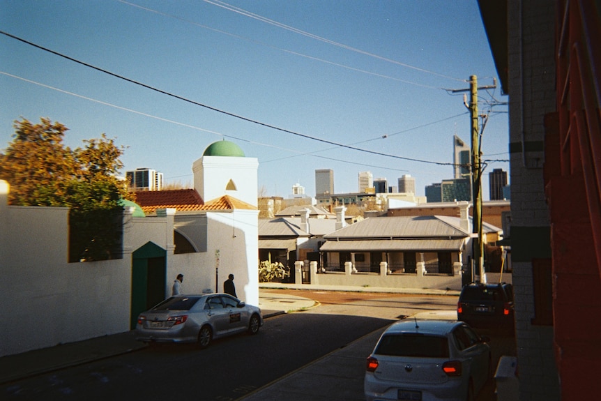 A mosque dome is lit by sunlight, with power line sweeping across the frame and cars in the dark foreground