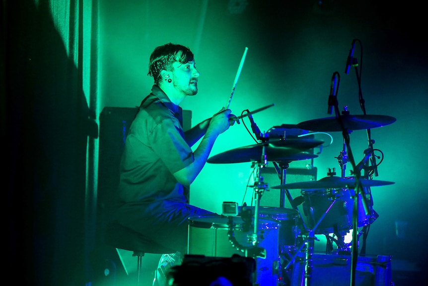 Young man plays drums under green lights