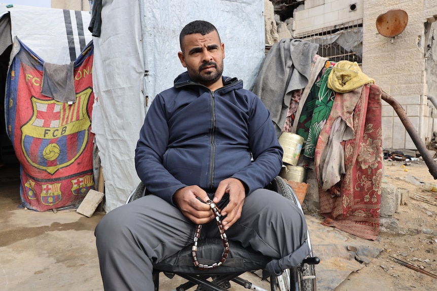 A man sitting outdoors in front of a dishevelled camp, one leg amputated below the knee.