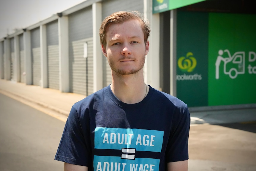 A portrait of a young man standing outside a supermarket loading bay.