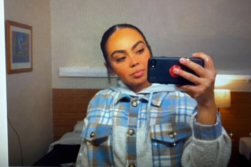 A young, dark-haired woman in a flannel shirt takes a selfie.