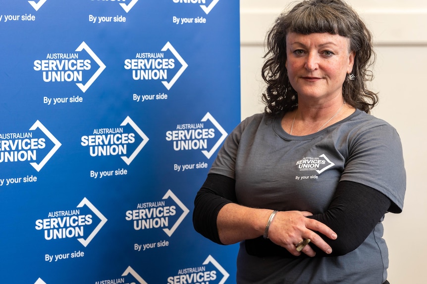 A woman with brown hair stands in front of a panel with Australian Services Union branding. 
