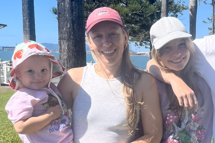 A woman holds a toddler, standing next to a girl.