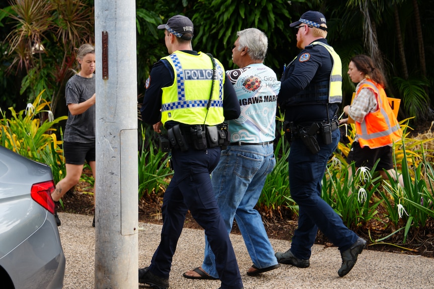 Two police officers escort a man along a footpath.
