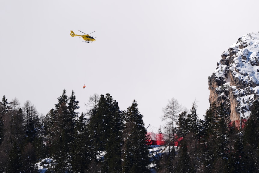 A helicopter flies over trees with a stretcher hanging under it