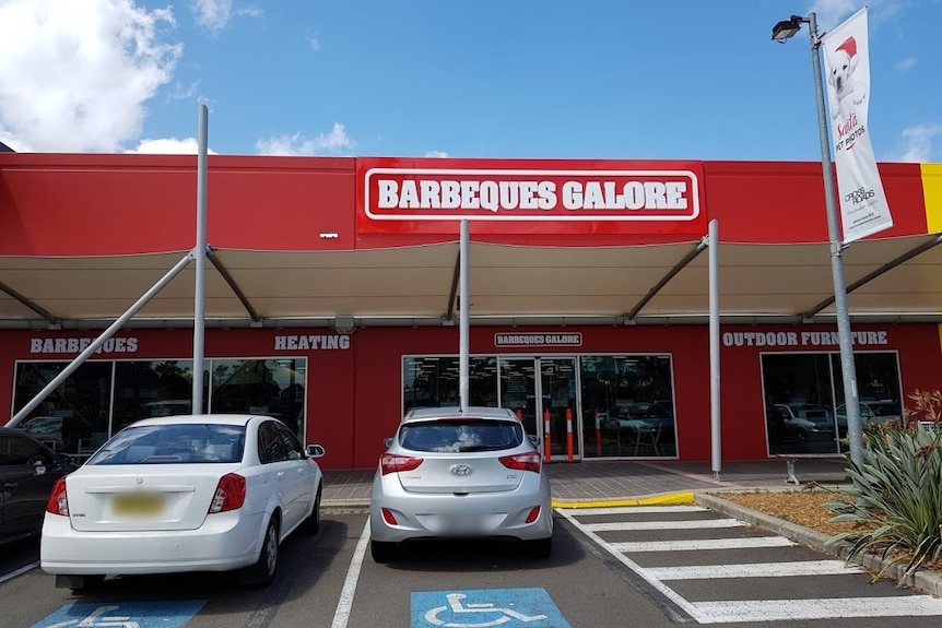 A shop with red signage that says barbeques galore and cars parked out the front.