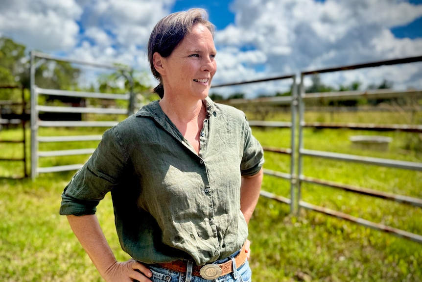 A woman stands hands on hips, looking out towards a paddock.