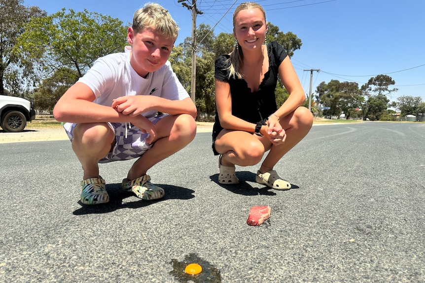 A boy and a girl crouch on the road with a smashed egg in front of them