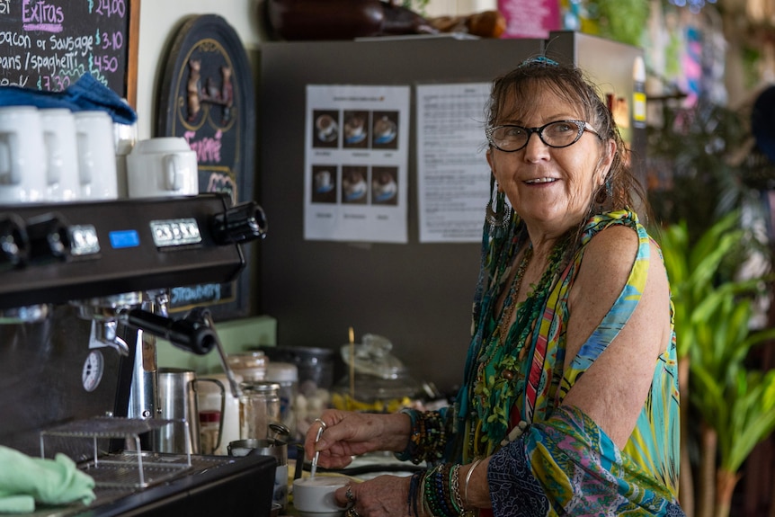 A woman looks off-camera with a smile while steaming milk for a coffee.