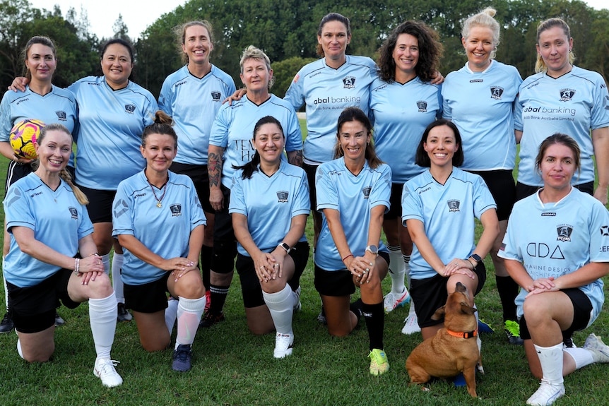 Members of an over 25s women's football team line up in two rows and smile for a team photo.