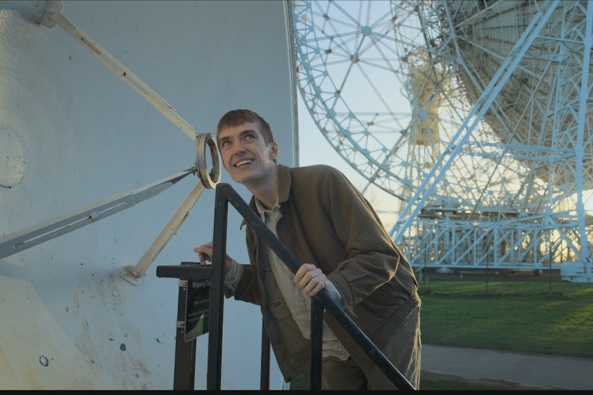 Francis crouches down to place an ear against a satellite dish