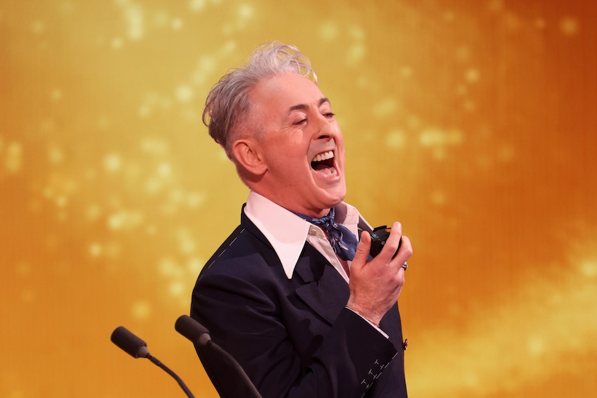 A man in a suit screams into a mic.