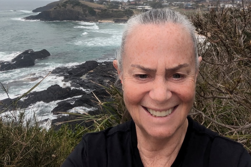  Jann Alhafny, takes a selfie with her grey hair pulled back, standing on a coastal cliff.