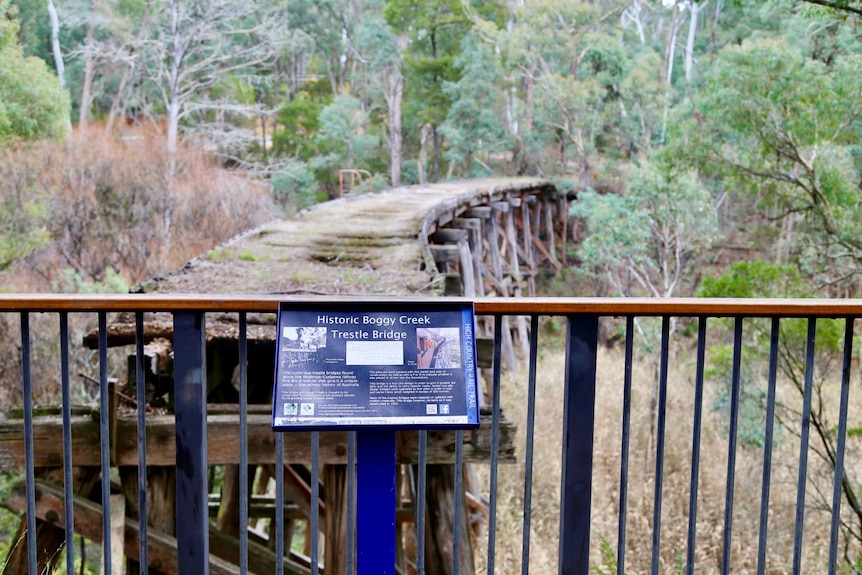 an information sign with an old, mossy wooden trestle bridge in the background
