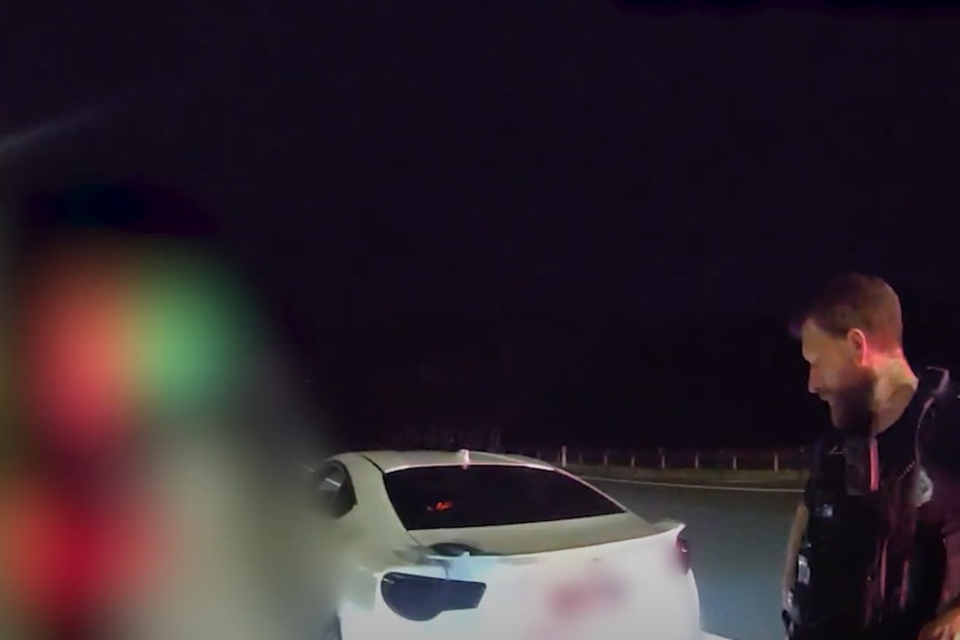 Policeman speaking to man, blurred, behind sports car