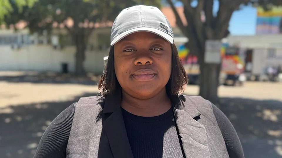 A head and shoulders image of a woman in a grey cap and black top. She is staring into the camera.