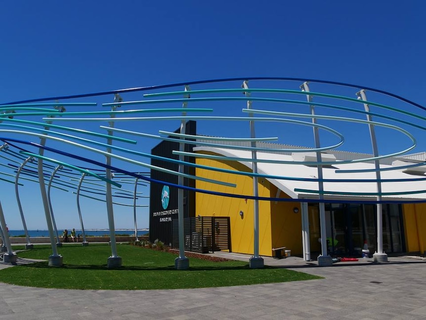 A large sculprute outside a bright-coloured building near the ocean.