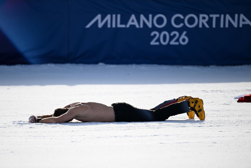 A man without a shirt on lies face down in the snow