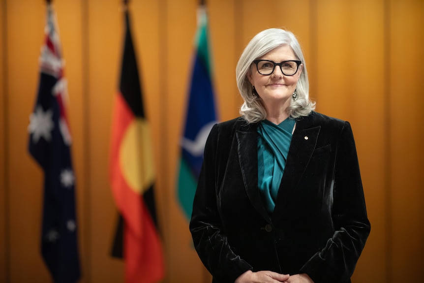 Sam Mostyn stands in front of the Australian, Aboriginal and Torres Strait Islander flags