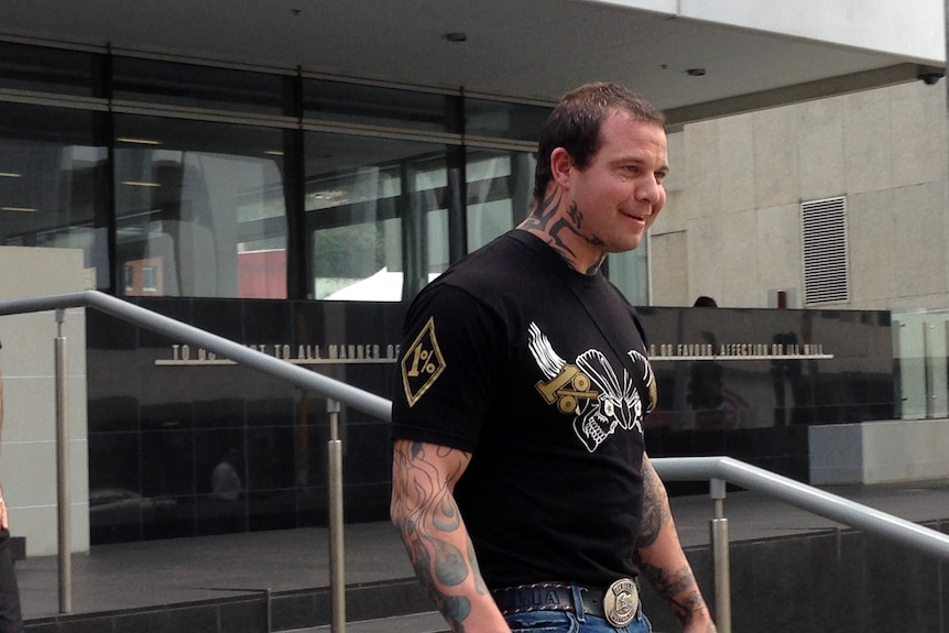 A man named David Pye has tattoos and smiles as he walks down stairs. 